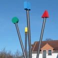 Vier unterschiedlich gefärbte, senkrechte Metallstangen als modernes Kunstwerk unter klarem Himmel.