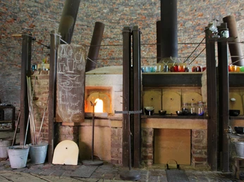 Ofen in der Glashütte Gernheim Ein brennender Glasofen in Gernheim, umgeben von traditionellen Werkzeugen und Glaskunst.