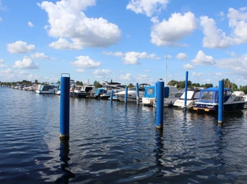 Boote liegen an blauen Stegen vor Anker, mit Wolken am Himmel und ruhigem Wasser darunter.