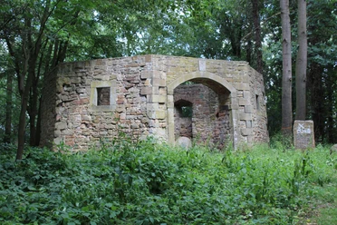 Naturumgebene Ruine einer alten Mühle mit moosbewachsenen Steinen und einem offenen Bogendurchgang.