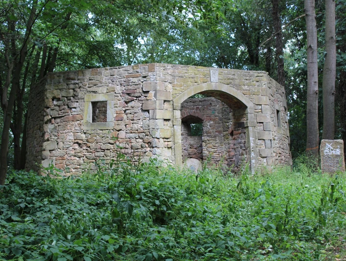 Naturumgebene Ruine einer alten Mühle mit moosbewachsenen Steinen und einem offenen Bogendurchgang.