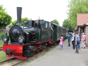 Dampflok mit roten Details am Bahnhof, Passagiere beim Einsteigen, Bäume im Hintergrund.Steam locomotive with red details at the station, passengers boarding, trees in the background.Damplokomotiv med røde detaljer på stationen, passagerer stiger på, træer i baggrunden.Stoomlocomotief met rode details op het station, instappende passagiers, bomen op de achtergrond.