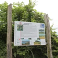 Informationsschild über den Naturlehrpfad Im Röden Stolzenau zwischen zwei Holzpfosten vor grüner Vegetation.