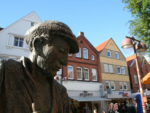 Bronzestatue eines Glasbläsers in Nienburg, umrahmt von historischen Gebäuden im Hintergrund.