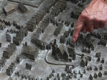 Ein Finger deutet auf ein detailliertes Stadtmodell aus Bronze, das Gebäude und Straßen darstellt.