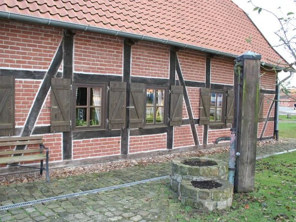 Ole Schüne Drakenburg Fachwerkgebäude mit Holzstrukturen, Backsteinmauerwerk und Brunnen im Vordergrund. Ländliche Atmosphäre.