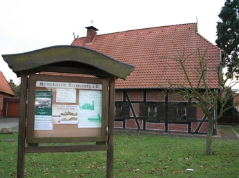 Fachwerkhaus mit Infobereich vorne, rotes Ziegeldach, umgeben von Rasen und Pflasterweg.