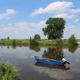 Weser bei Petershagen Ein ruhiges Gewässer mit einem blauen Boot im Vordergrund, umgeben von grüner Flusslandschaft.