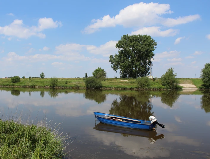Weser bei Petershagen Ein ruhiges Gewässer mit einem blauen Boot im Vordergrund, umgeben von grüner Flusslandschaft.