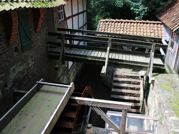 Plaggen Mühle Döhren Historische Wassermühle in Döhren mit hölzernem Steg, Ziegelwänden und bewaldeter Umgebung.
