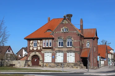 Backsteingebäude mit roten Ziegeldächern, großen Fenstern und einem Storchennest auf dem Schornstein.