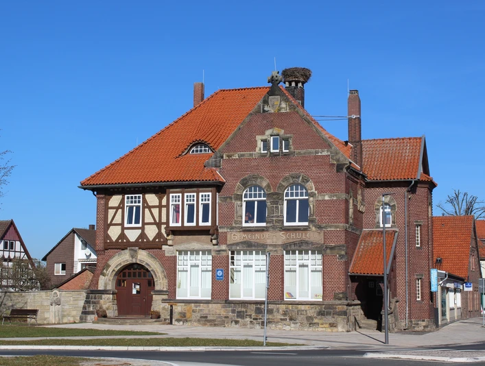 Stadt Rehburg-Loccum Polizei Backsteingebäude mit roten Ziegeldächern, großen Fenstern und einem Storchennest auf dem Schornstein.