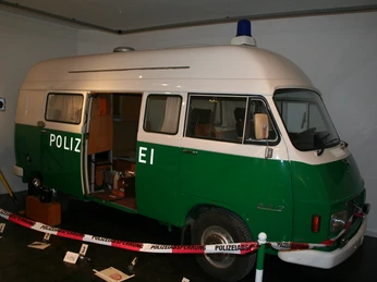 Polizeibus im Polizeimuseum Ein grüner Polizei-Van im Museum, mit offener Tür und Ausstellungsstücken um ihn herum.A green police van in the museum, with the door open and exhibits around it.En grøn politibil på museet med åben dør og udstillingsgenstande rundt om.Een groene politiebus in het museum, met de deur open en tentoonstellingsstukken eromheen.