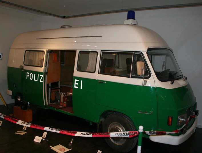 Polizeibus im Polizeimuseum Ein grüner Polizei-Van im Museum, mit offener Tür und Ausstellungsstücken um ihn herum.A green police van in the museum, with the door open and exhibits around it.En grøn politibil på museet med åben dør og udstillingsgenstande rundt om.Een groene politiebus in het museum, met de deur open en tentoonstellingsstukken eromheen.