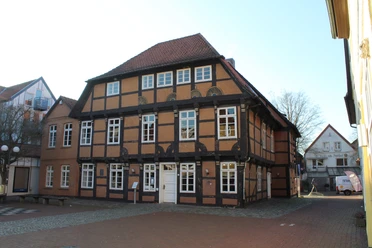 Fachwerkhaus mit rotem Ziegeldach und weißen Fensterrahmen, umgeben von gepflasterten Wegen.