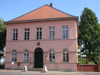 Quaet-Faslem-Haus Ein rosafarbenes, zweigeschossiges Gebäude mit rotem Dach und großen, weißen Sprossenfenstern.