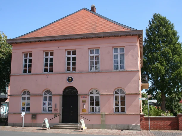 Quaet-Faslem-Haus Ein rosafarbenes, zweigeschossiges Gebäude mit rotem Dach und großen, weißen Sprossenfenstern.