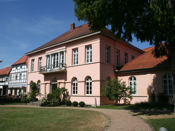 Quaet-Faslem-Haus Historisches Herrenhaus in Pastellrosé mit großen Fenstern, umgeben von gepflegten Gartenanlagen.