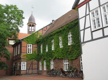 Rathaus Rückansicht Eine Backsteinfassade mit grünem Efeubewuchs, weiß gestrichenen Fenstern und einem Kirchturm im Hintergrund.A brick façade with green ivy, white-painted windows and a church tower in the background.En murstensfacade med grøn efeu, hvidmalede vinduer og et kirketårn i baggrunden.Een bakstenen gevel met groene klimop, witgeschilderde ramen en een kerktoren op de achtergrond.