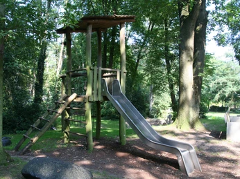 Rathauspark Achim: Spielplatz mit Holzklettergerüst, Rutsche und grüner Umgebung; kinderfreundlich.