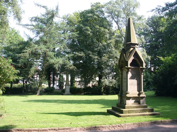 Rathauspark Achim Ein steinerner Obelisk steht auf einer Rasenfläche in einem von Bäumen umgebenen Park in Achim.
