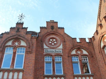 Das Foto zeigt die rote Backsteinfassade der historischen Bauschule Rehburg mit verzierten Fenstern.