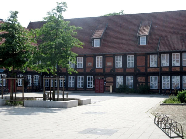 Historic half-timbered building Fresenhof with roof shingles, white window frames, striking red gate.