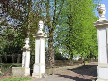 Historisches Eingangstor mit verzierten Säulen vor einer Allee, eingerahmt von lebendigem Grün.