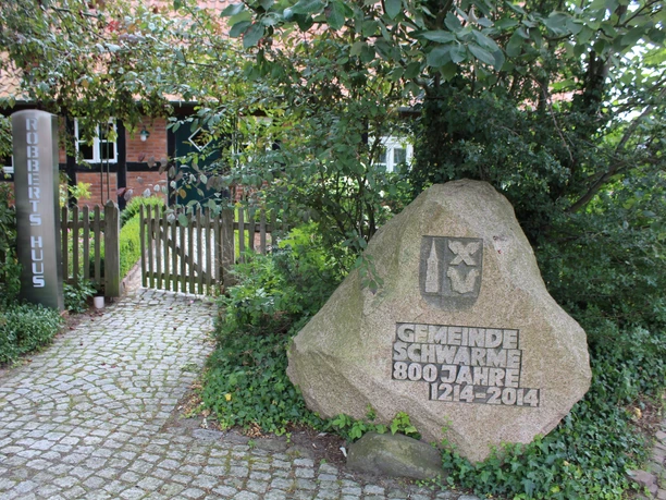 Robberts Huus Vor einem Backsteinhaus steht ein geschmückter Stein zum 800-jährigen Bestehen der Gemeinde Schwarme.