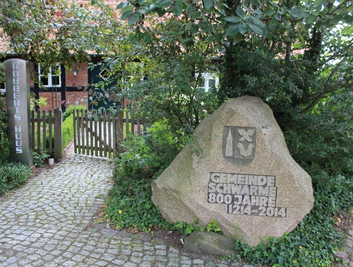 Robberts Huus Vor einem Backsteinhaus steht ein geschmückter Stein zum 800-jährigen Bestehen der Gemeinde Schwarme.