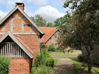 Historisches Fachwerkgebäude aus Backstein in einer grünen und blühenden Gartenlandschaft.