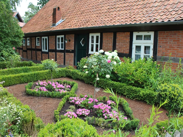 Robberts Huus Historisches Fachwerkhaus mit gepflegtem Garten und blühenden Beeten vor einer Backsteinfassade.