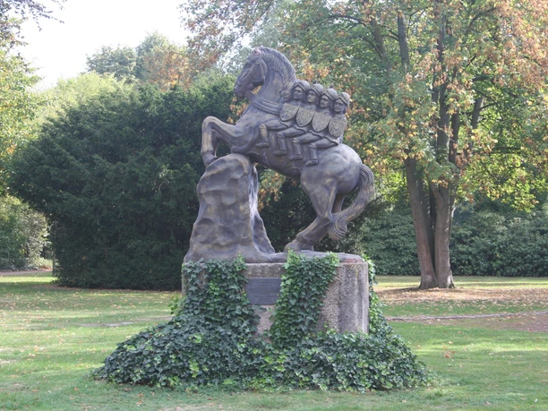 Bronzestatue eines aufgerichteten Pferdes mit starker Muskulatur auf einem mit Efeu bewachsenen Sockel.