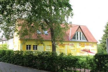 Ruderclub Stolzenau Ein gelb getünchtes Gebäude mit der Aufschrift "Ruderclub Stolzenau" und einem gemalten Ruderboot.