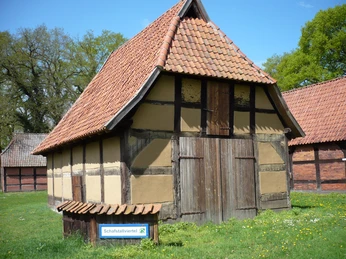 Traditioneller Fachwerkschafstall mit rotem Ziegeldach, umgeben von grüner Wiese im Schafstallviertel Hülsen.