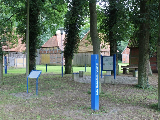 Inmitten großer Bäume befinden sich historische Schafställe und Infotafeln im Schafstallviertel.