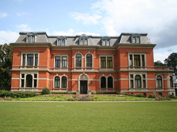Etelsen Castle with red brick, symmetrical design and a well-tended lawn in the foreground.