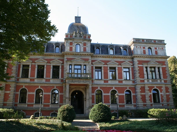 Brick façade with turrets and bay windows, surrounded by well-tended gardens in front of Etelsen Castle.