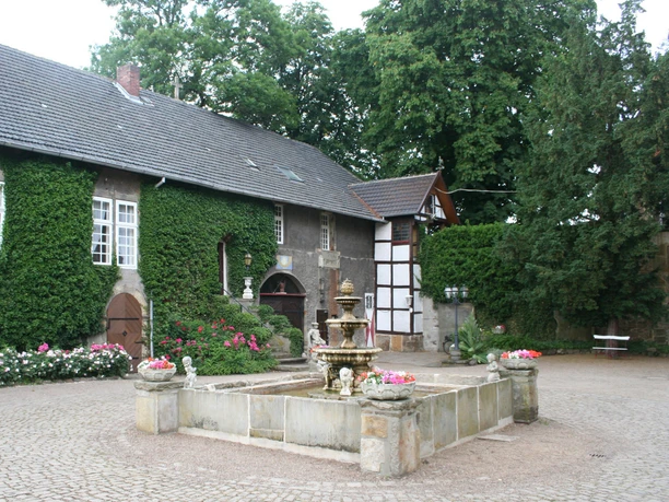 Ein steinerner Brunnen mit Wasserspeiern im Innenhof, umgeben von alten Gebäuden und grünen Bäumen.
