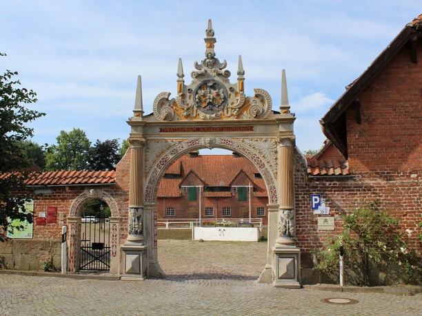 Prächtiges Tor mit figürlichen Verzierungen, flankiert von historischen Backsteinbauten.