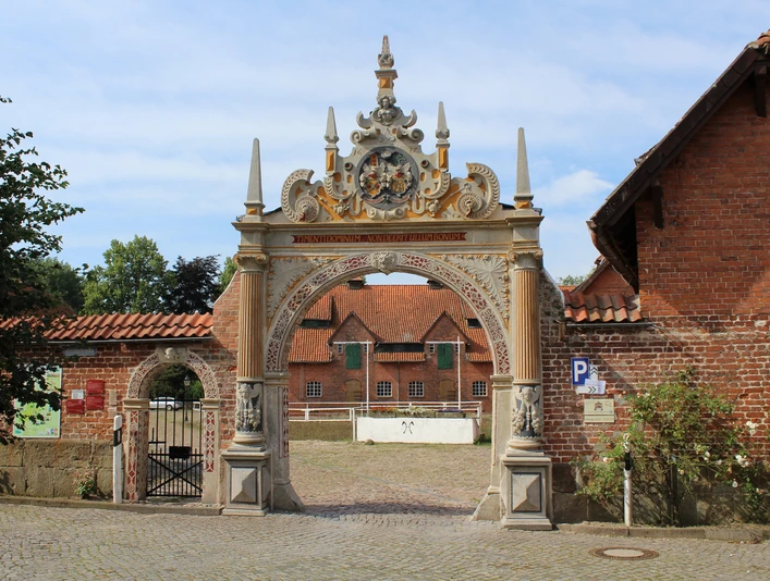 Prächtiges Tor mit figürlichen Verzierungen, flankiert von historischen Backsteinbauten.