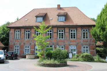 Ein traditionelles Fachwerkgebäude mit roten Ziegeln in Bruchhausen-Vilsen, umgeben von Grün.