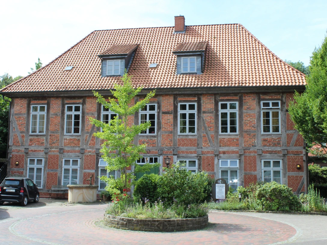 Ein traditionelles Fachwerkgebäude mit roten Ziegeln in Bruchhausen-Vilsen, umgeben von Grün.