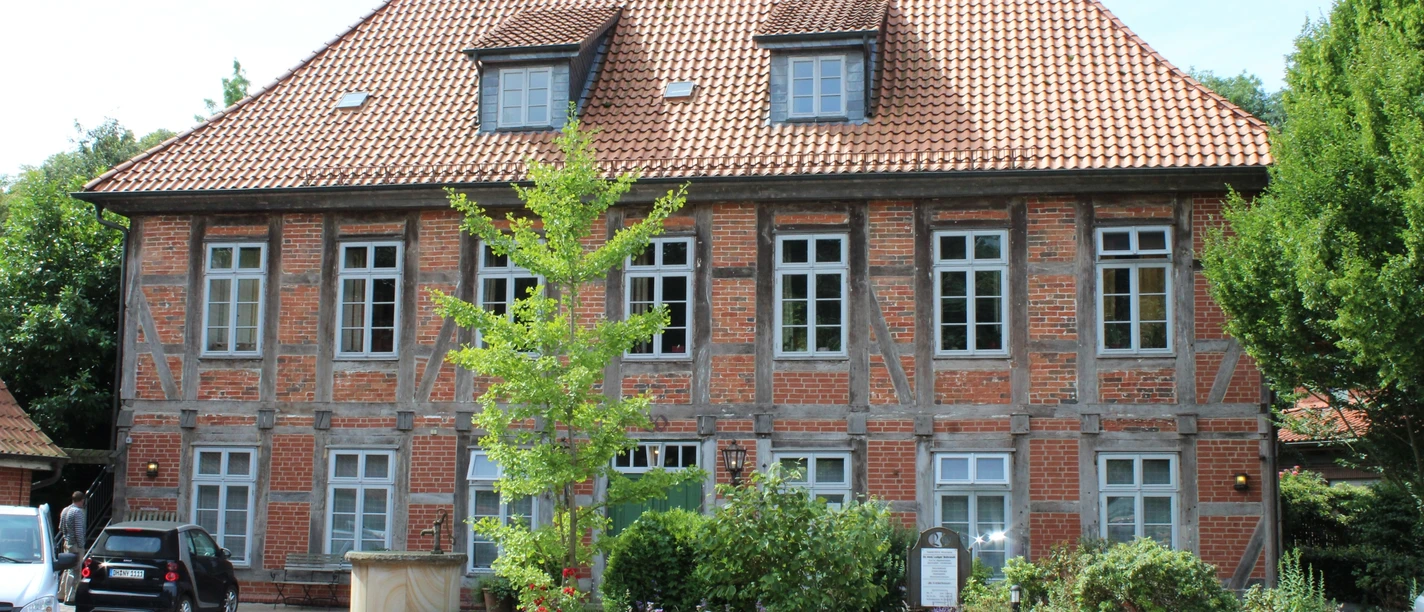 Ein traditionelles Fachwerkgebäude mit roten Ziegeln in Bruchhausen-Vilsen, umgeben von Grün.