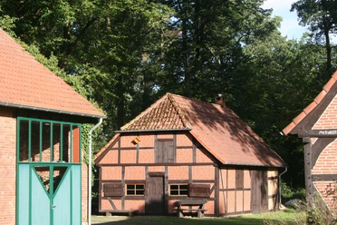 Historische Scheune mit Fachwerk und rotem Ziegeldach, umgeben von Bäumen in ruhiger Umgebung.