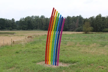 Skulptur Am Ende des Regenbogens Eine bunte Skulptur aus gebogenen Streben in Regenbogenfarben steht auf einer grünen Wiese.