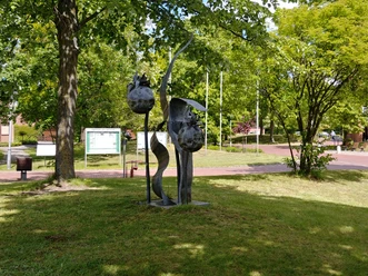 Skulptur aus Metall, zeigt stilisierte Beeren in einem Park mit Bäumen und Informationstafel.