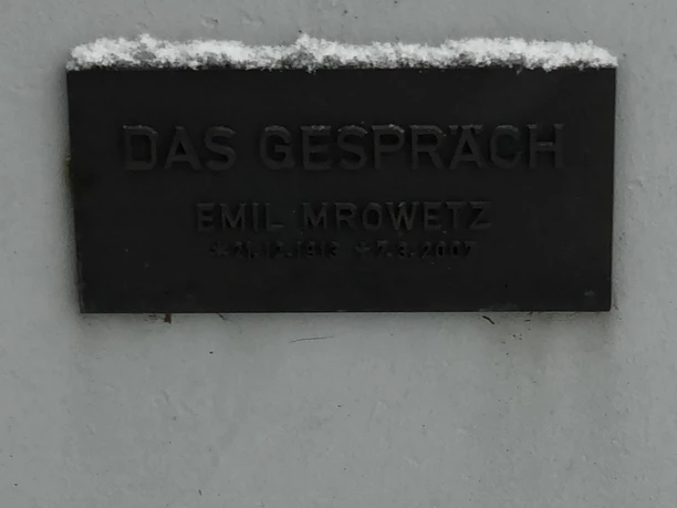 Tafel mit der Inschrift "Das Gespräch" von Emil Mrowetz, beleuchtet durch Schneeakzente oben.