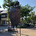 Skulptur Entfaltung Zwei abstrahierte Figuren in moderner Metallskulptur stehen vor einer Apotheke im städtischen Ambiente.