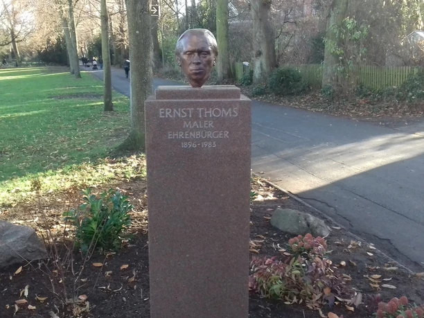 Bronzeskulptur von Ernst Thoms auf einem Sockel im Grünen, gewidmet als Maler und Ehrenbürger.